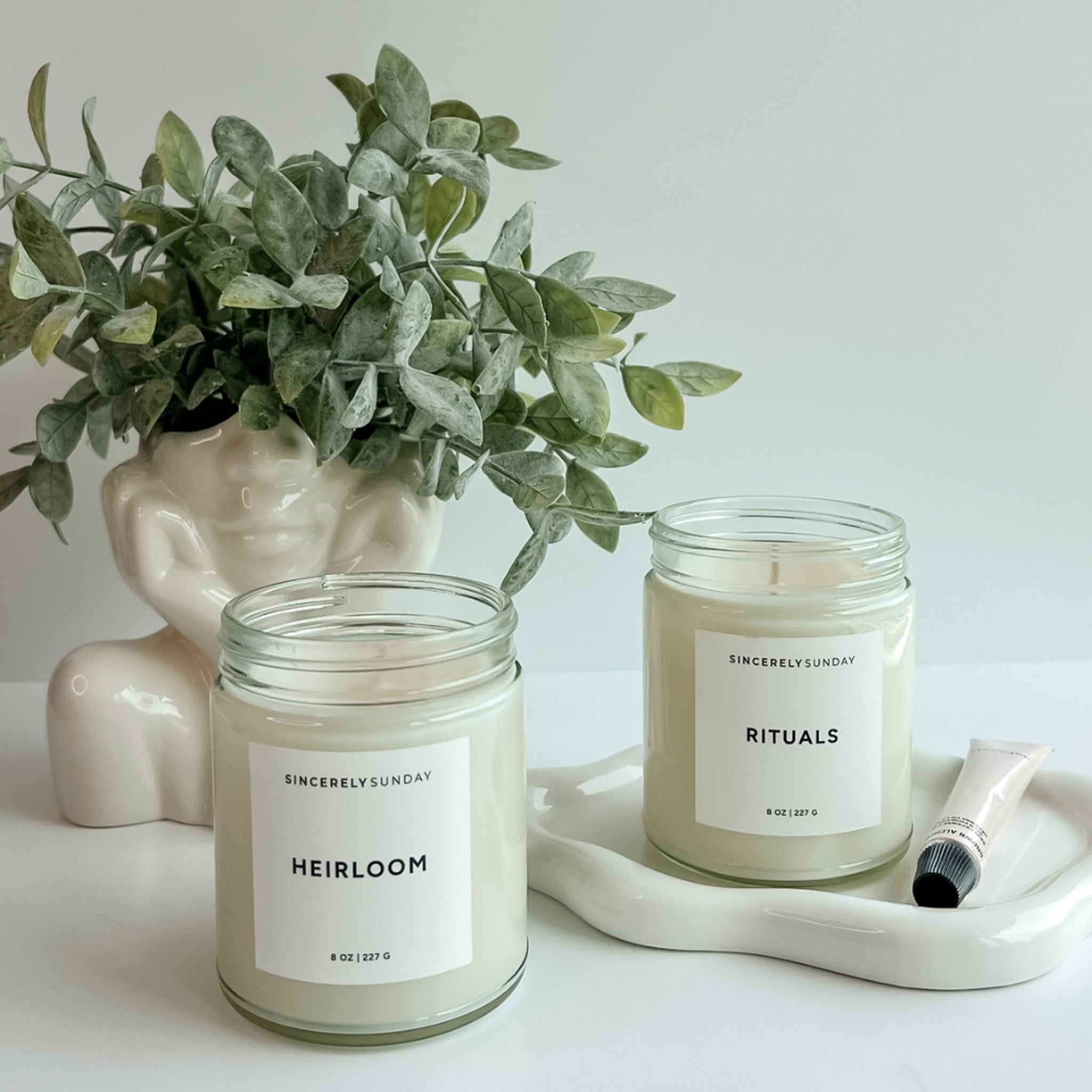 Heirloom and Rituals candles on a white cloud-shaped tray, styled with a plant and lip gloss nearby.