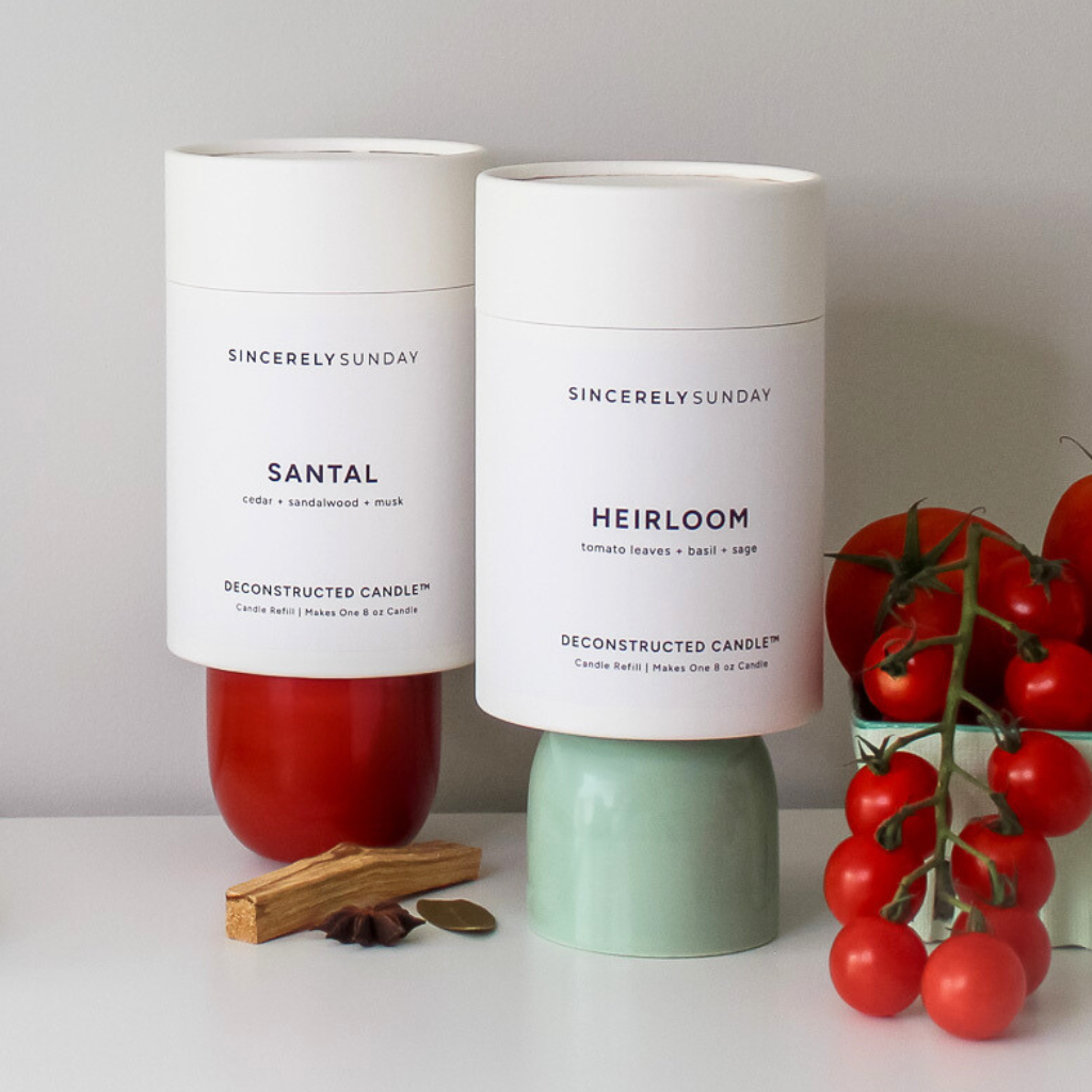 Two candle refills placed on colorful cups beside a bowl of tomatoes on the vine