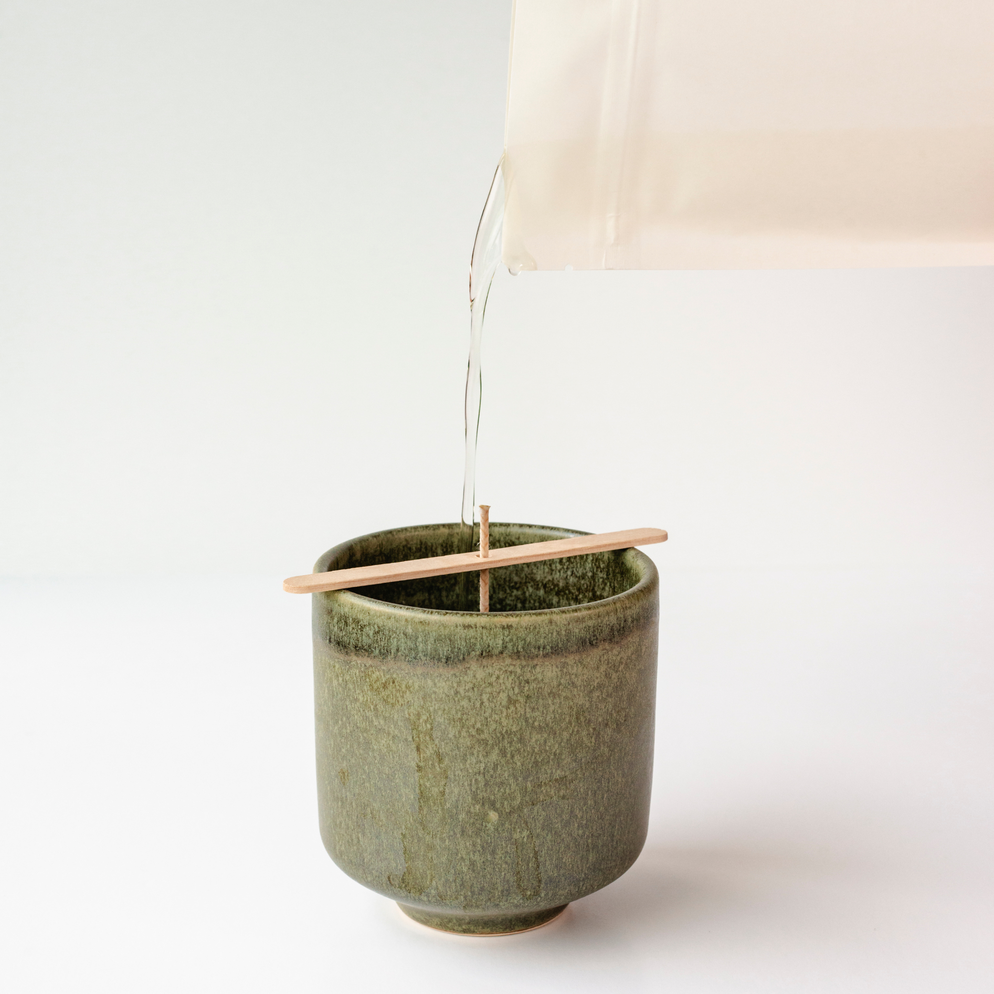 Wax from a white pouch being poured into a dark green vessel on a white background.