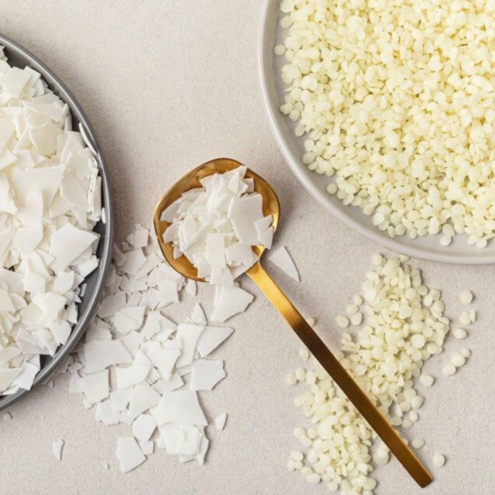 Top-down view of two bowls containing different types of wax, with a spoon between them holding one of the waxes.