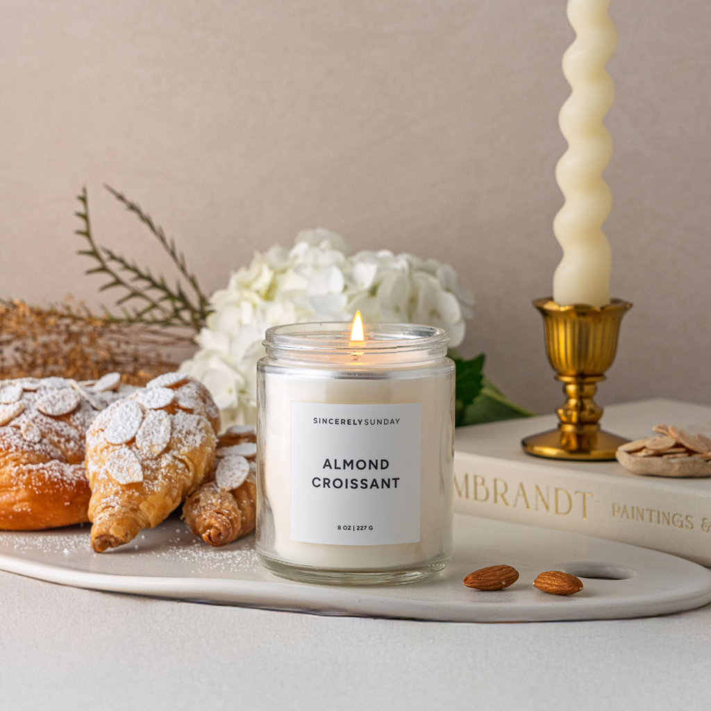 Candle labeled 'Almond Croissant' on a table with pastries and flowers