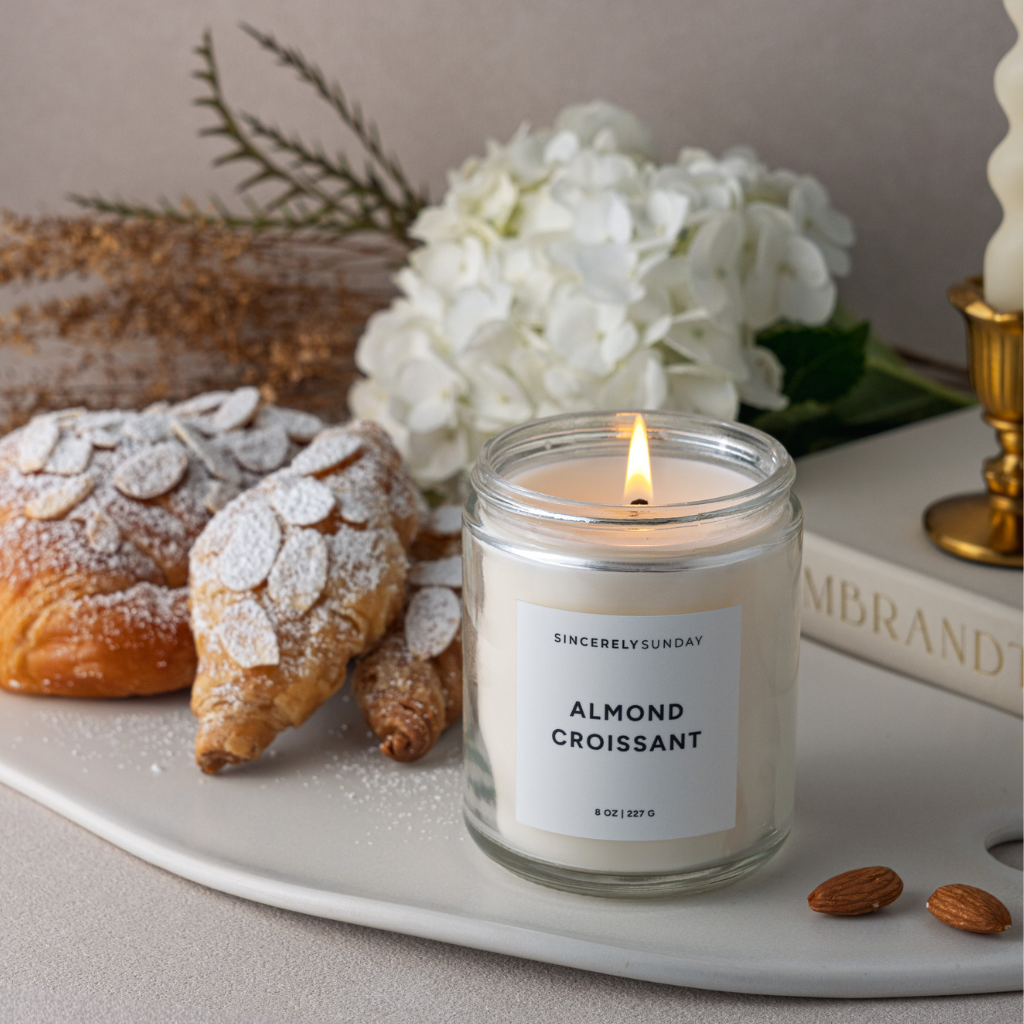 Candle labeled 'Almond Croissant' with pastries and flowers on a tray