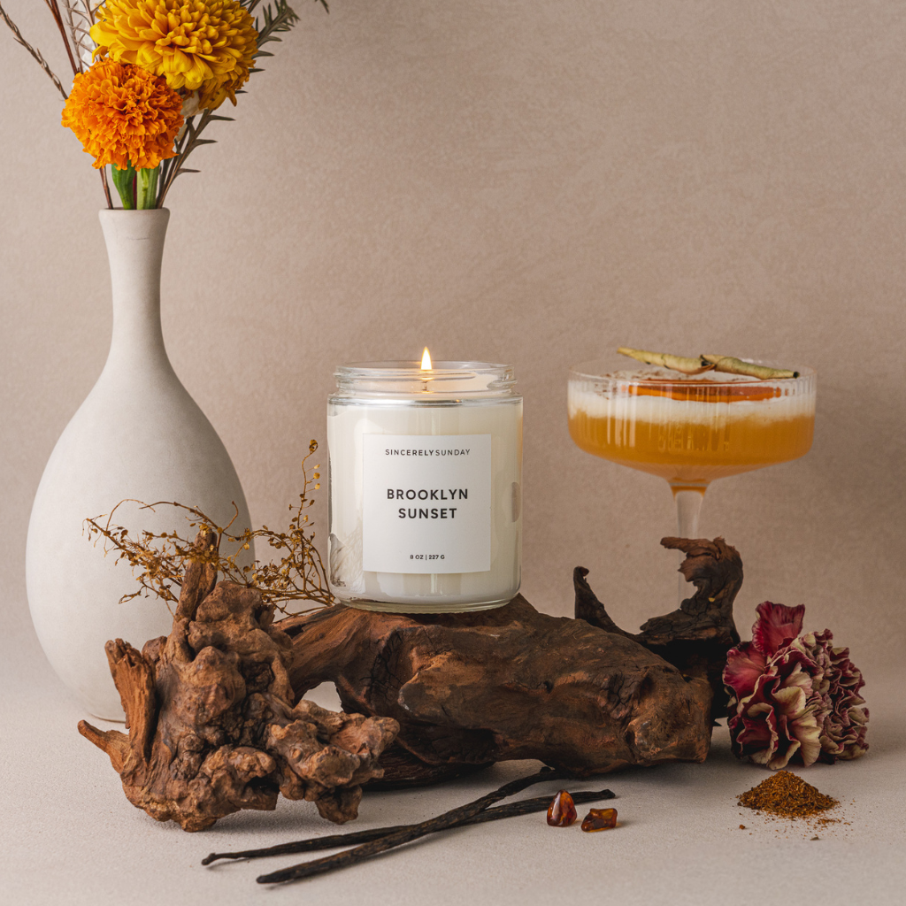 Candle labeled 'Brooklyn Sunset' with a cocktail and decorative elements on a neutral background