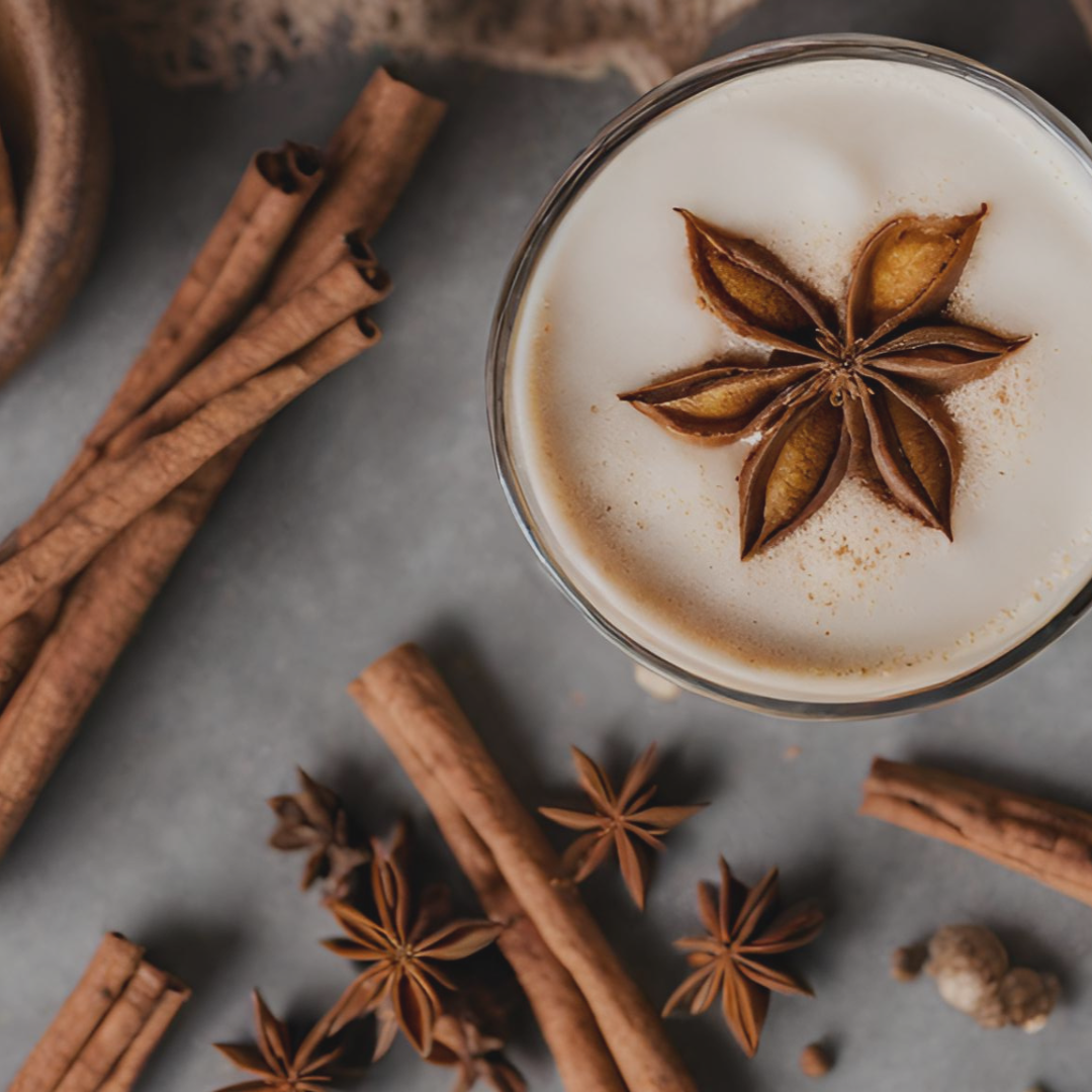 Cup of coffee with star anise on top, surrounded by cinnamon sticks and star anise on a gray surface.