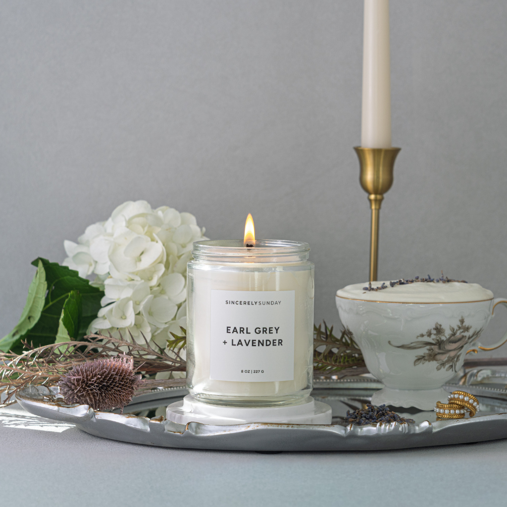 Candle labeled 'Earl Grey + Lavender' on a tray with flowers and a teacup.