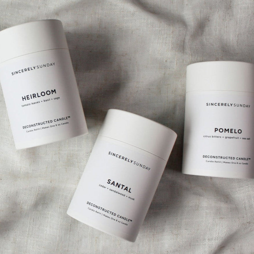 Three candle refill kits in white cylindrical paper tubes on a textured beige linen surface