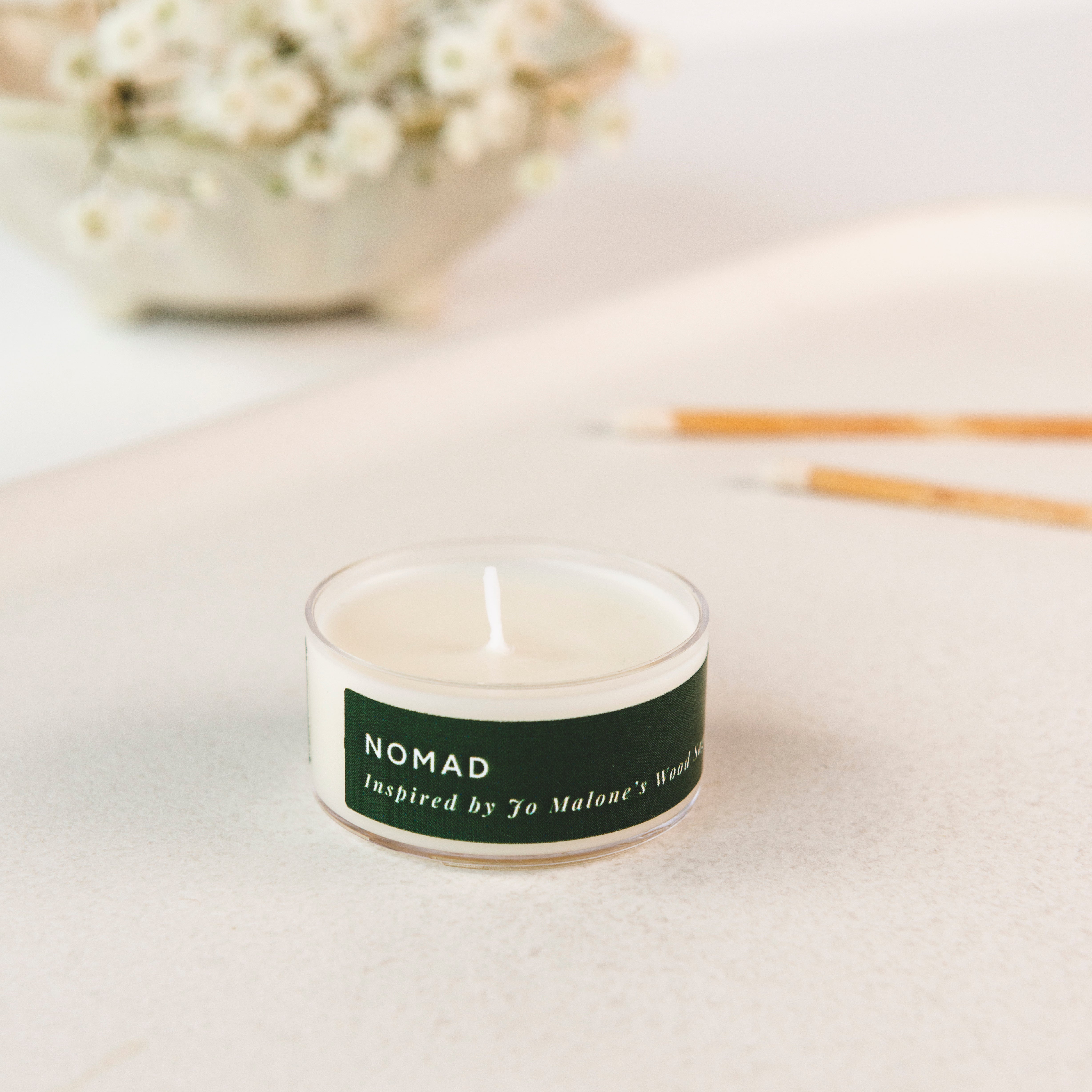 Tea light candle labeled 'Nomad' inspired by Jo Malone on a light surface with a blurred background