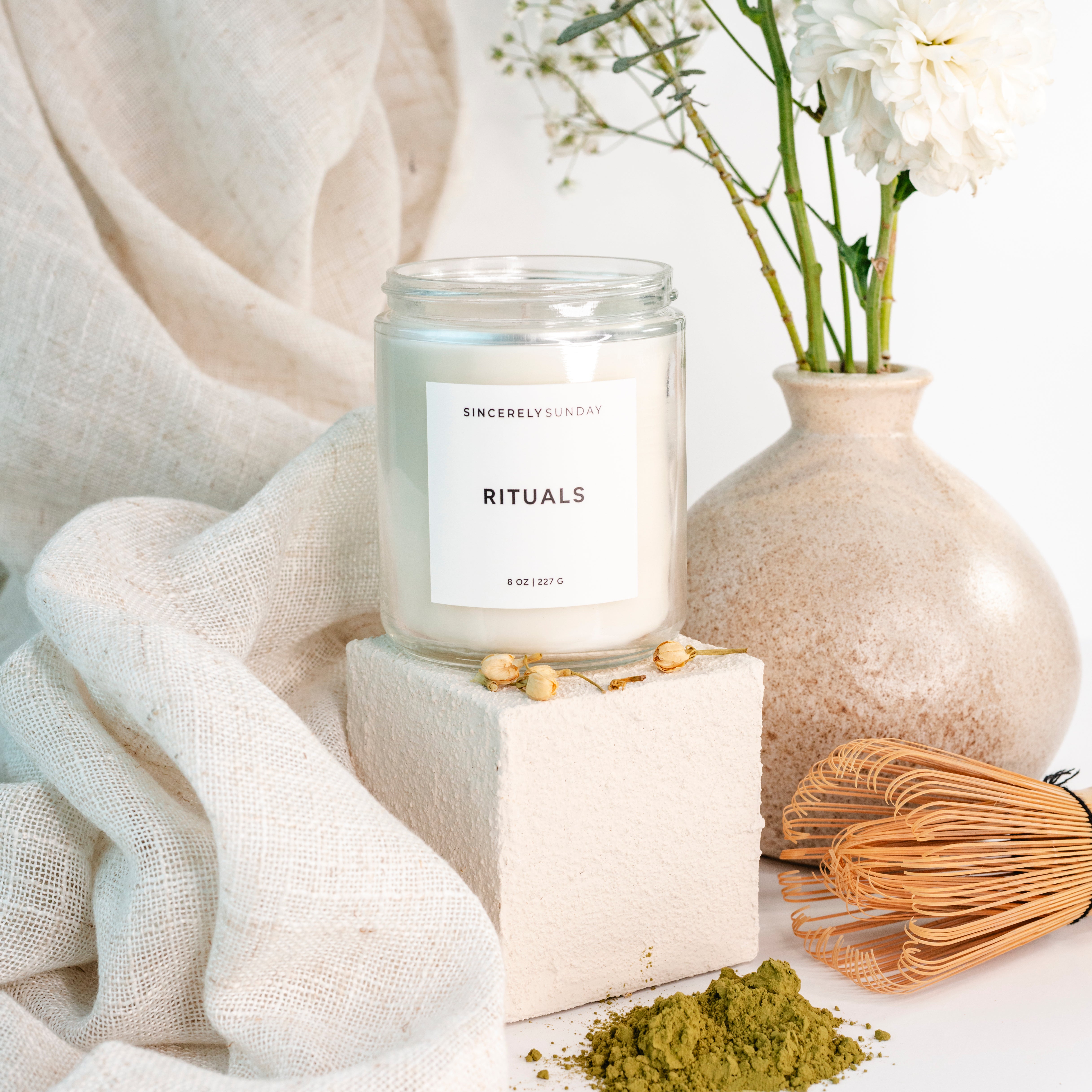 Candle labeled 'Rituals' with a vase of flowers and other decorative items on a light background