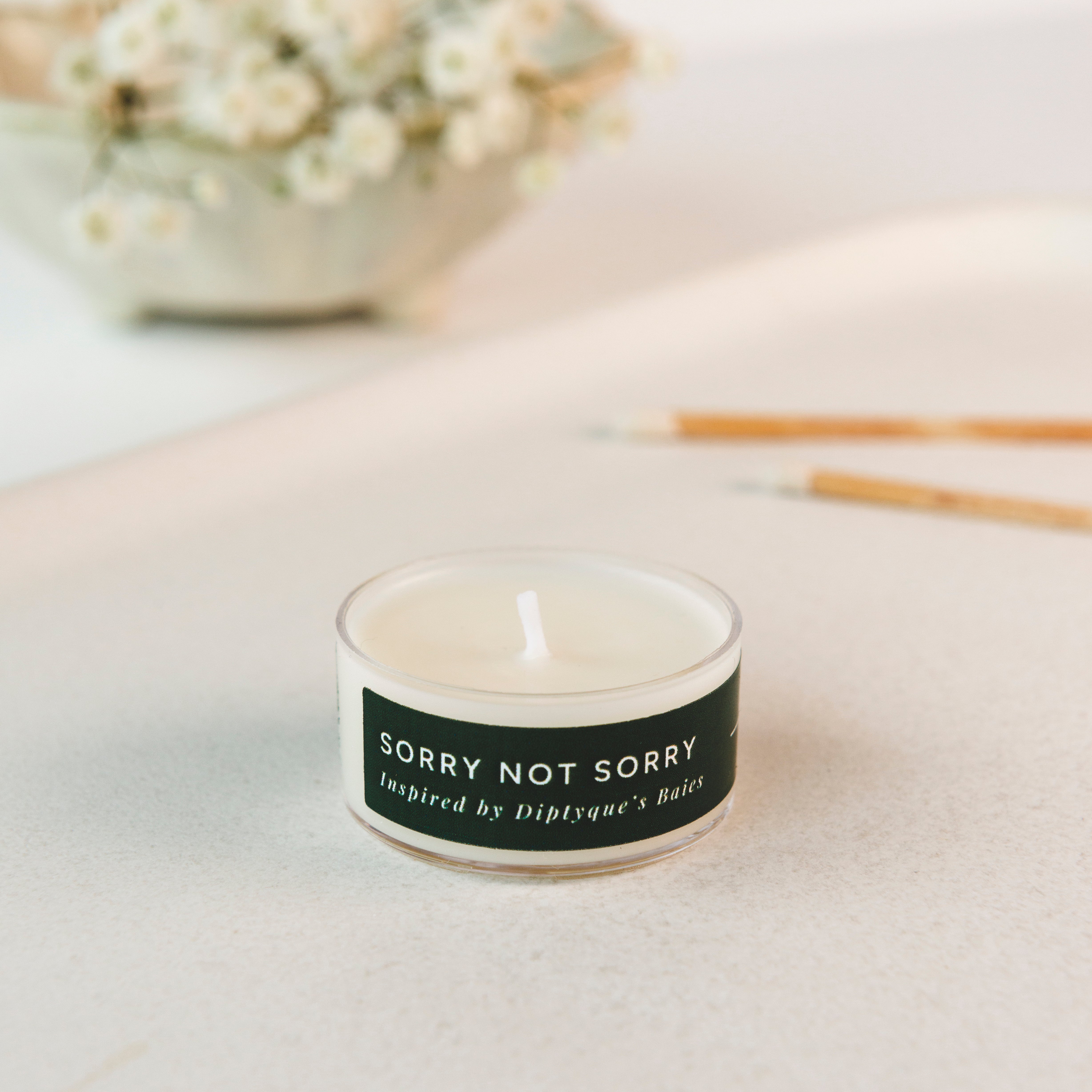 Tea light candle with a label 'Sorry Not Sorry' on a light surface with a blurred background