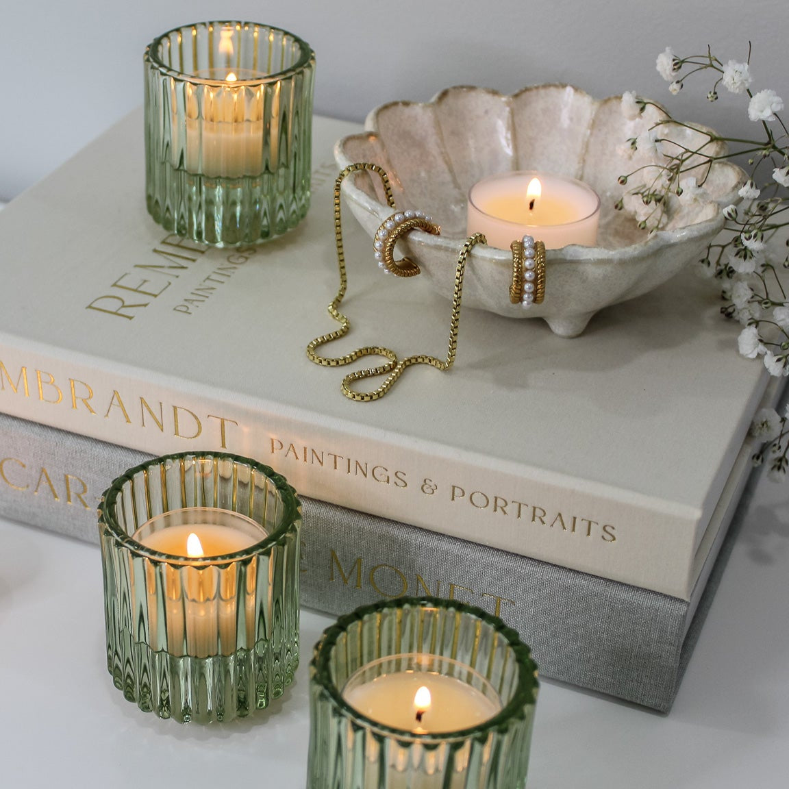 Green glass candle holders with lit candles on top of books
