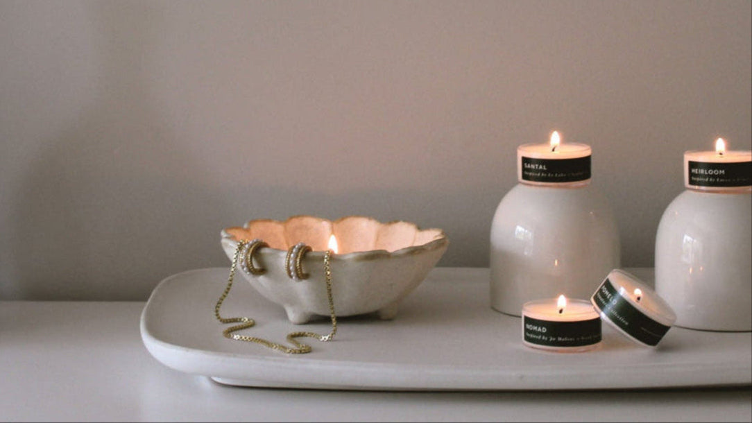 Four lit tea light candles on a tray beside a vase and scalloped ceramic dish with jewelry draped over it.