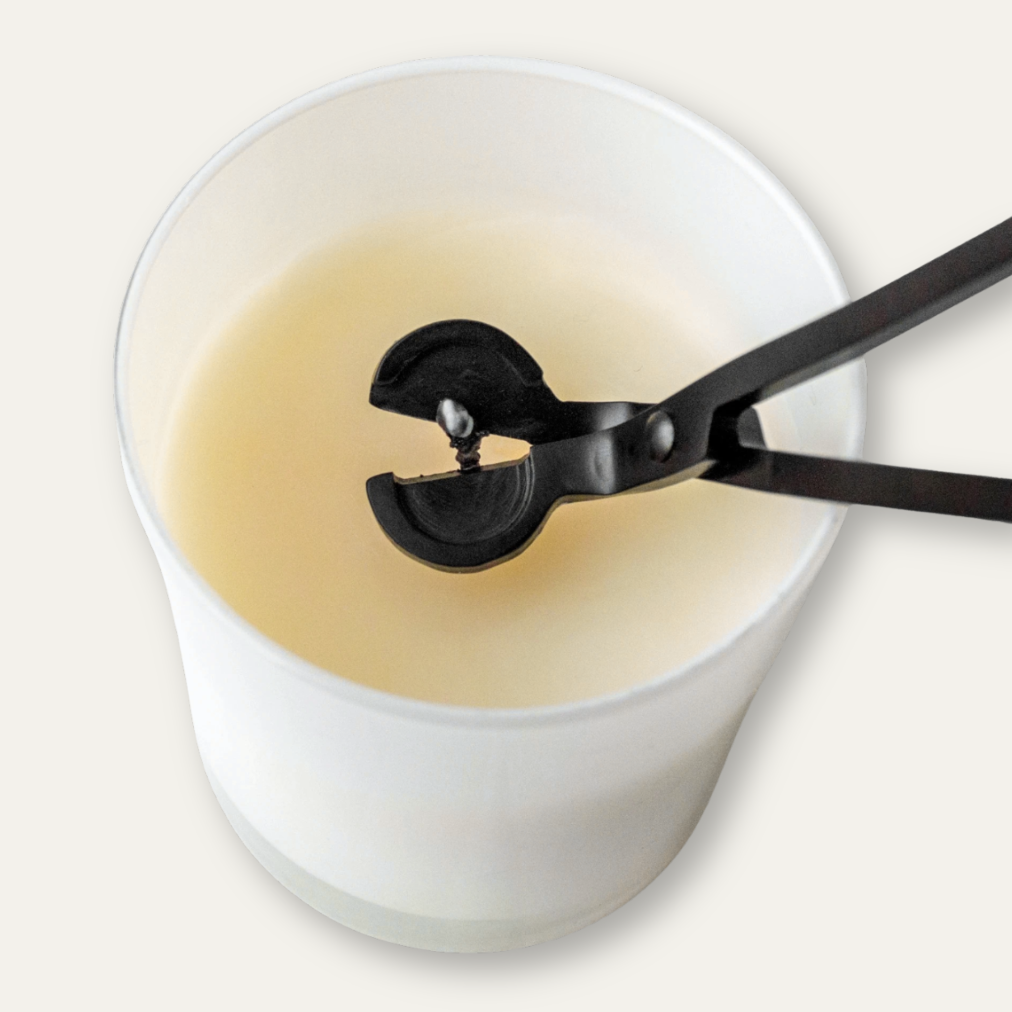 Black wick trimmer held over a white candle with black soot on the wick