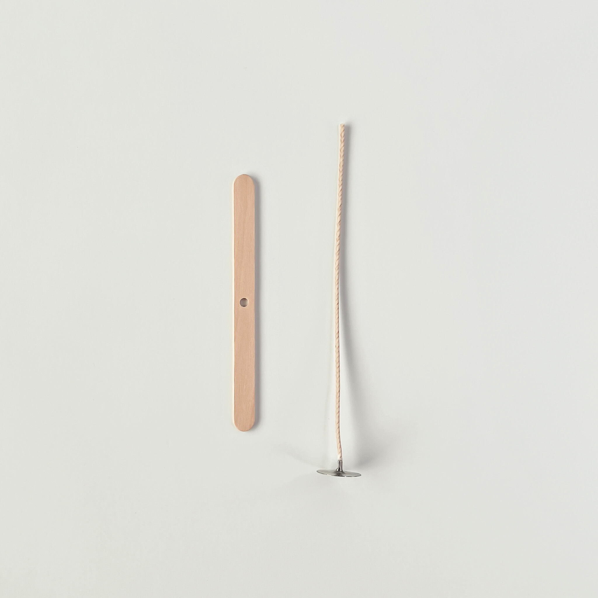 Wooden wick holder and candle wick on a light gray background