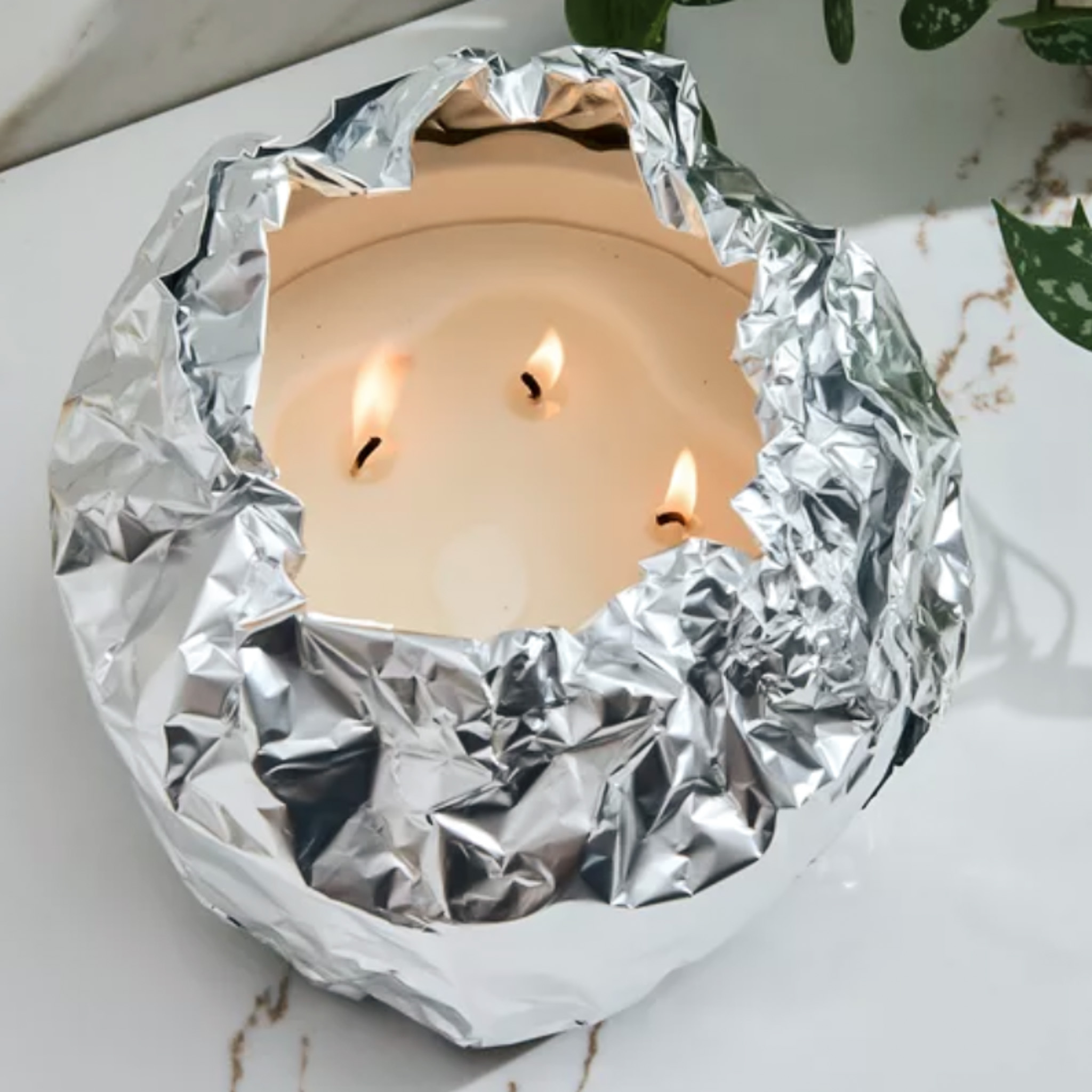 Lit candle wrapped in tinfoil on a white surface