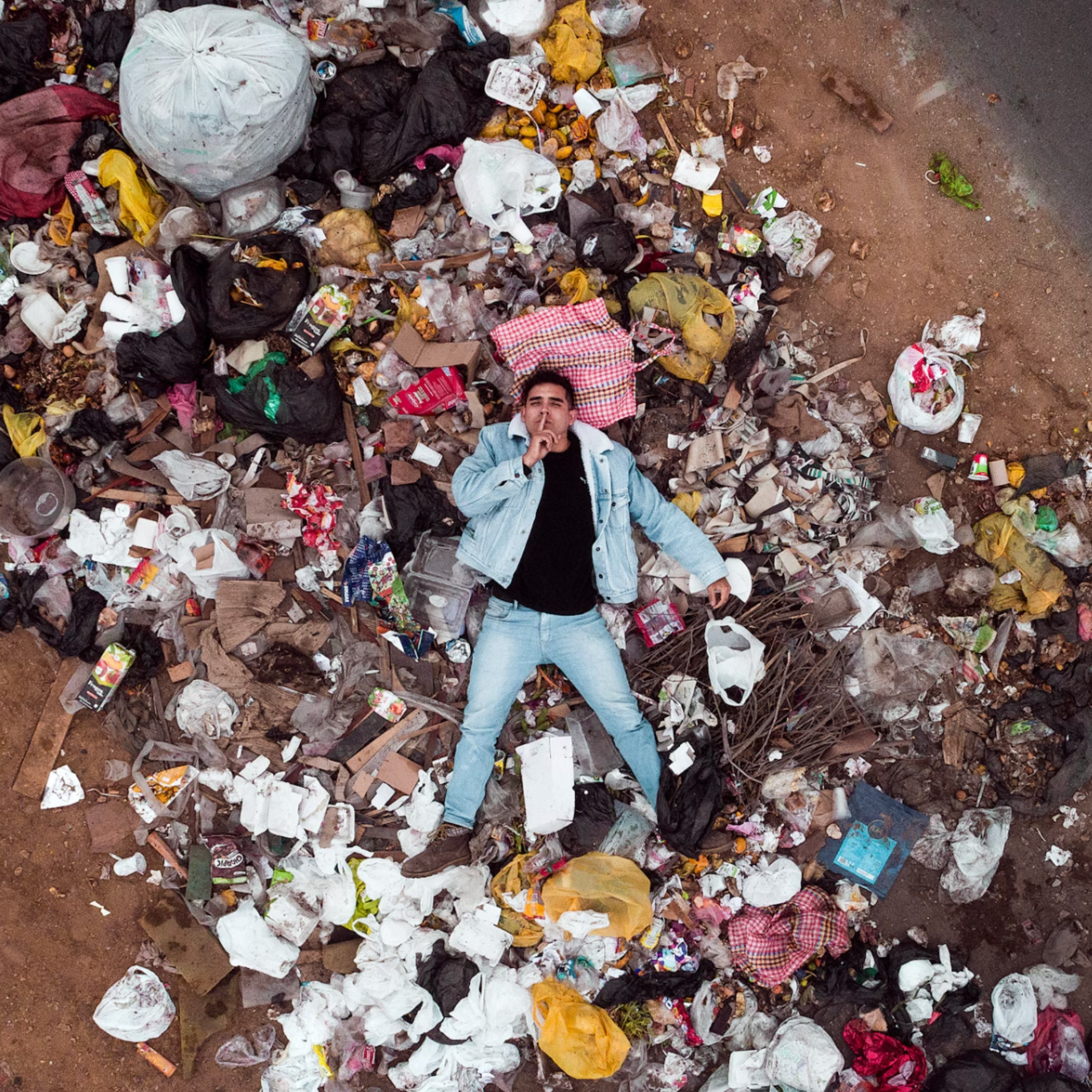 Top-down view of person lying amidst a pile of garbage and litter