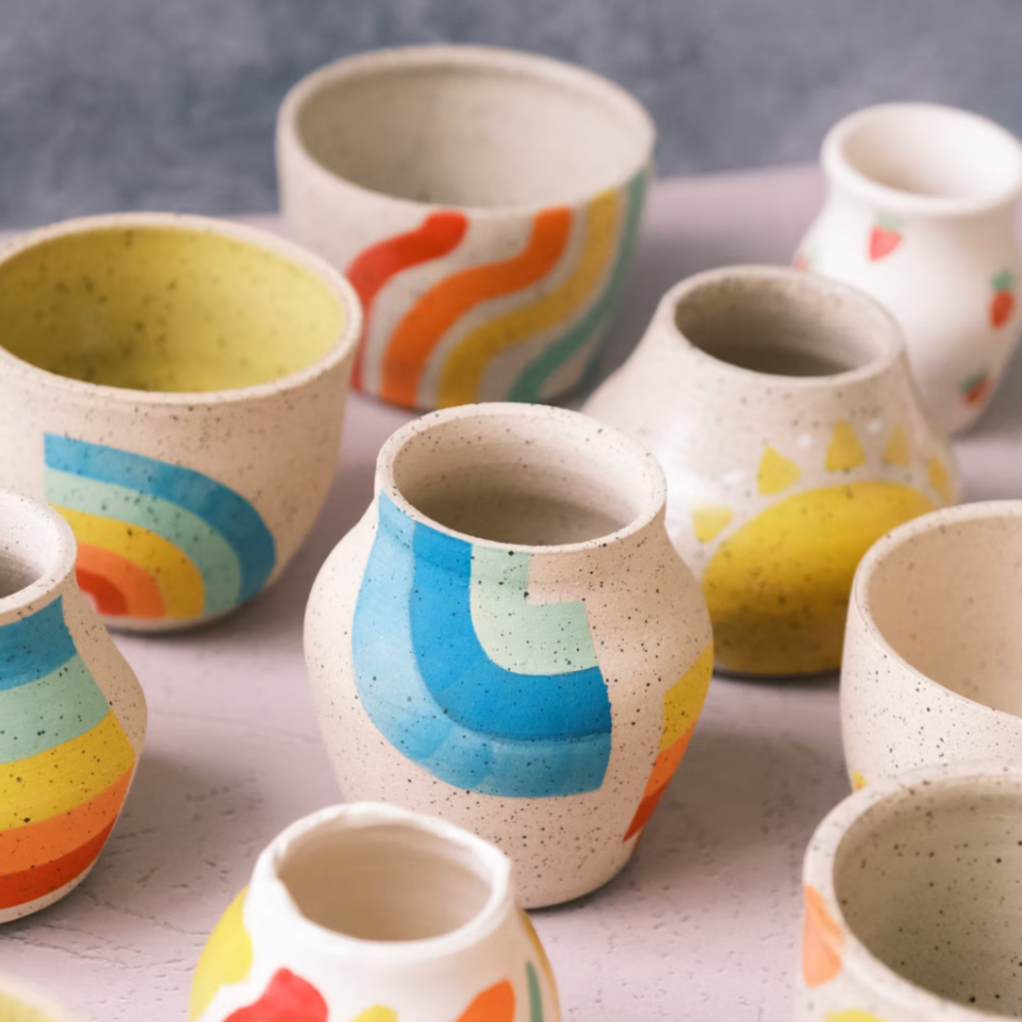 Collection of ceramic cups with colorful designs on a light background