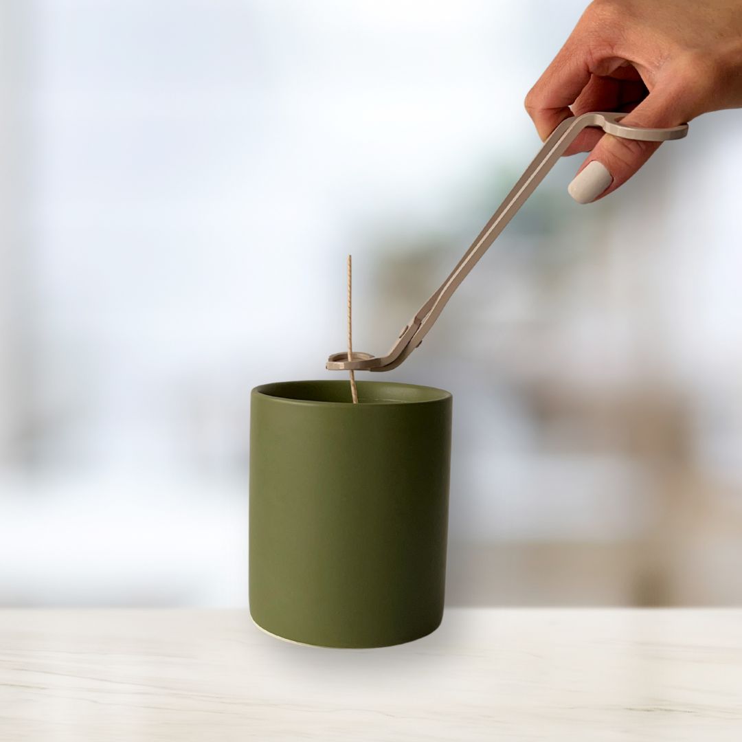 Using wick trimmer to trim cotton wick of freshly poured candle in sage green vessel, completing the candle-making process.