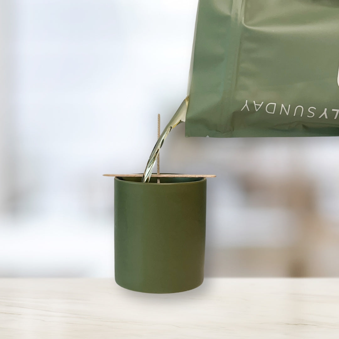 Pouring melted coconut-soy wax from a Sincerely Sunday Deconstructed Candle pouch into a sage green vessel.