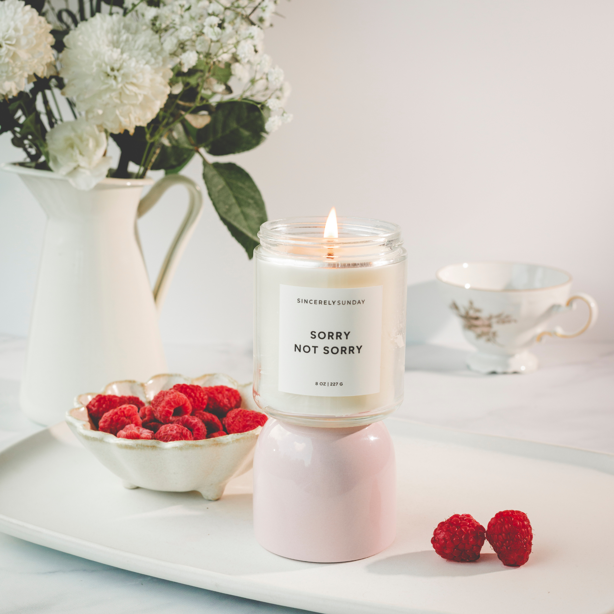 Candle labeled 'Sorry Not Sorry' on a table with flowers and raspberries