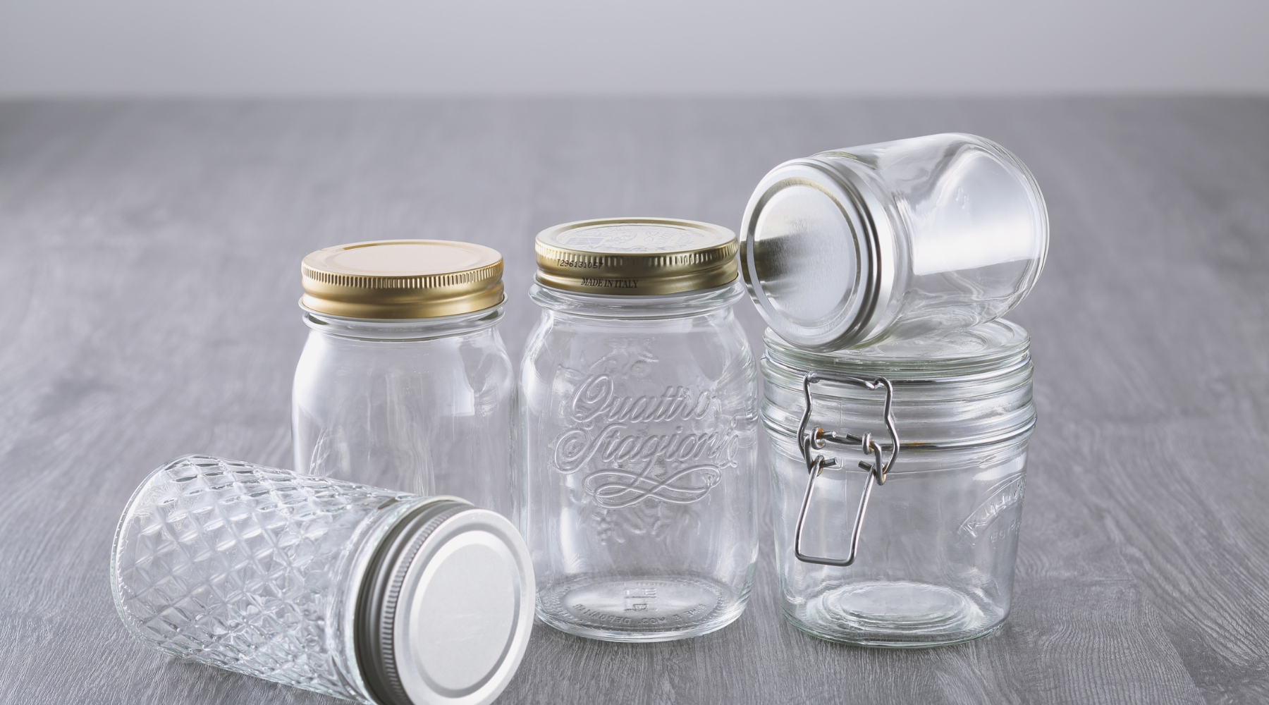 Several empty glass jars arranged on a gray tabletop, symbolizing the waste from throwaway culture and the potential for reuse through candle refills.
