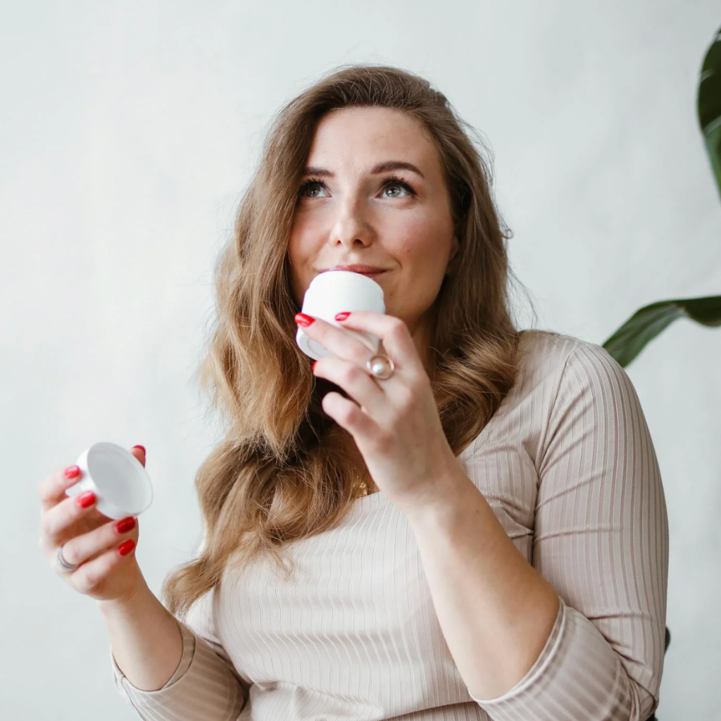 Woman holding a candle and smelling it with a plant in the background