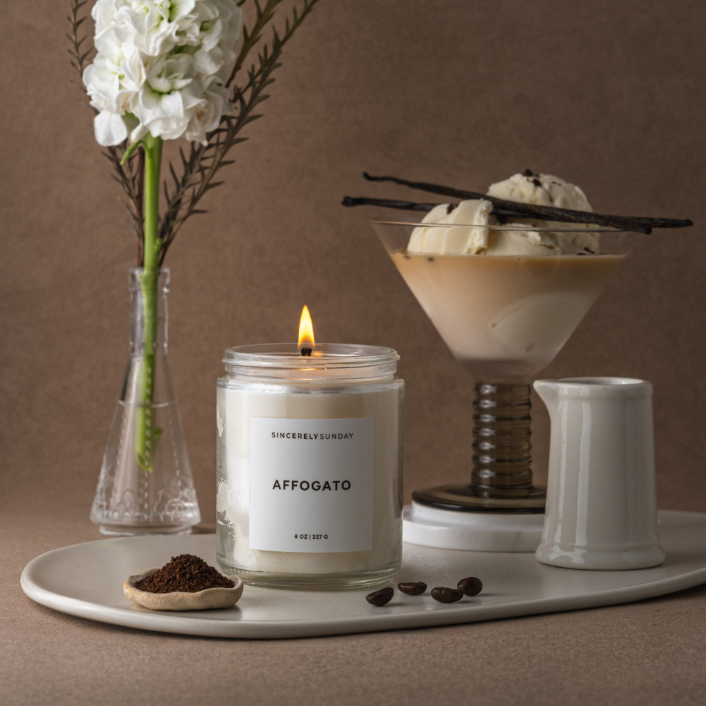 Candle labeled 'AFFOGATO' on a tray with flowers, coffee beans, and a dessert.
