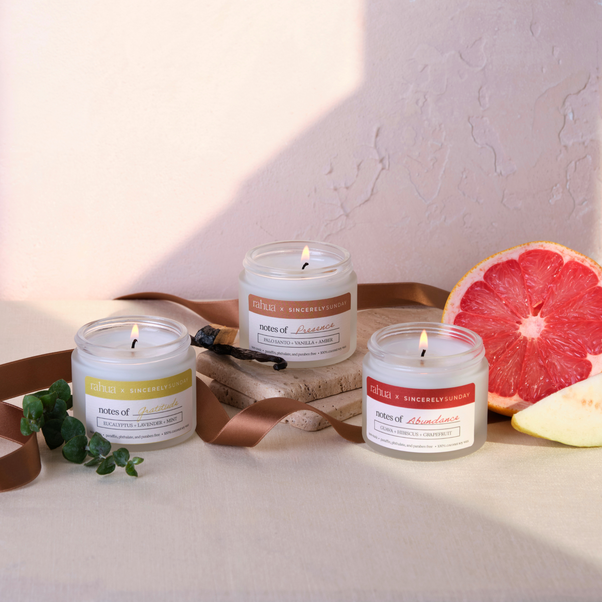 Three lit candles on a wooden tray with a pink grapefruit and green leaves on a light background