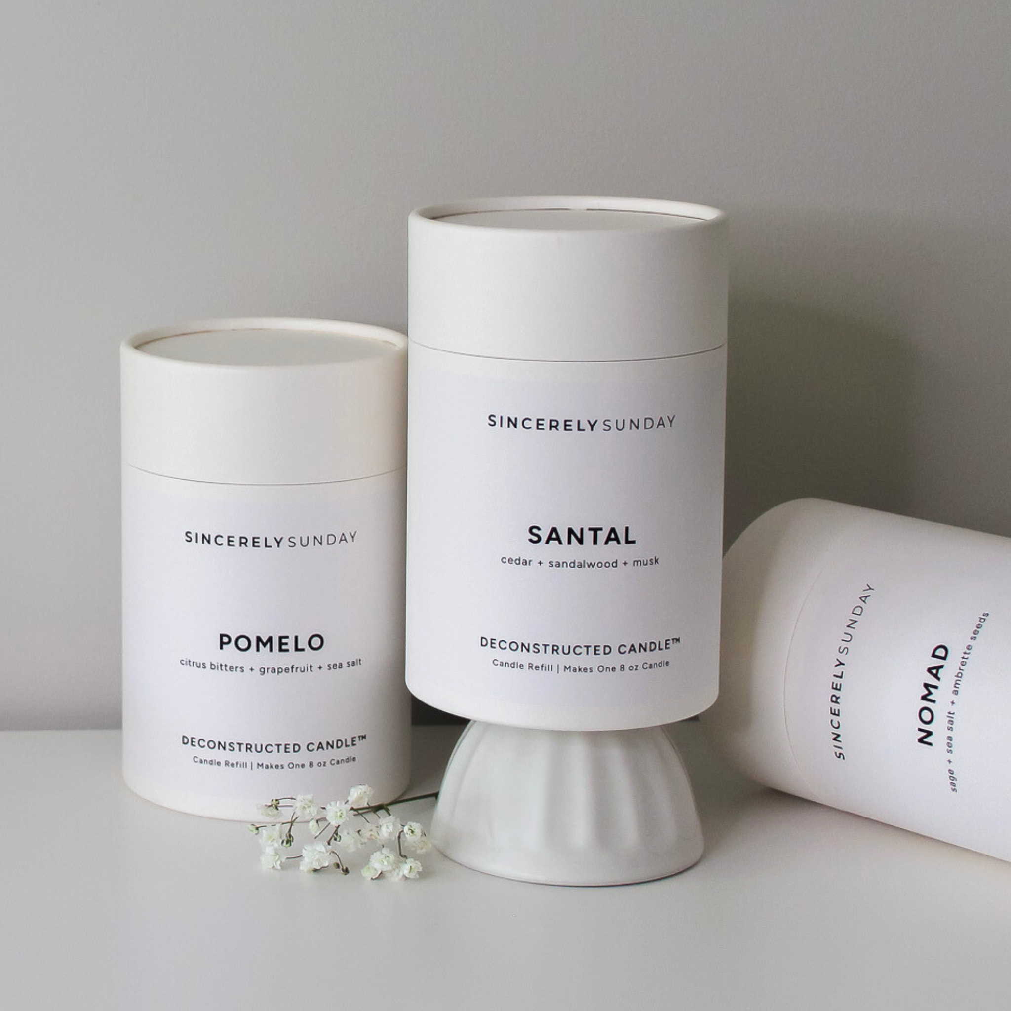 Three white cylindrical candle refill kits with labels on a gray surface