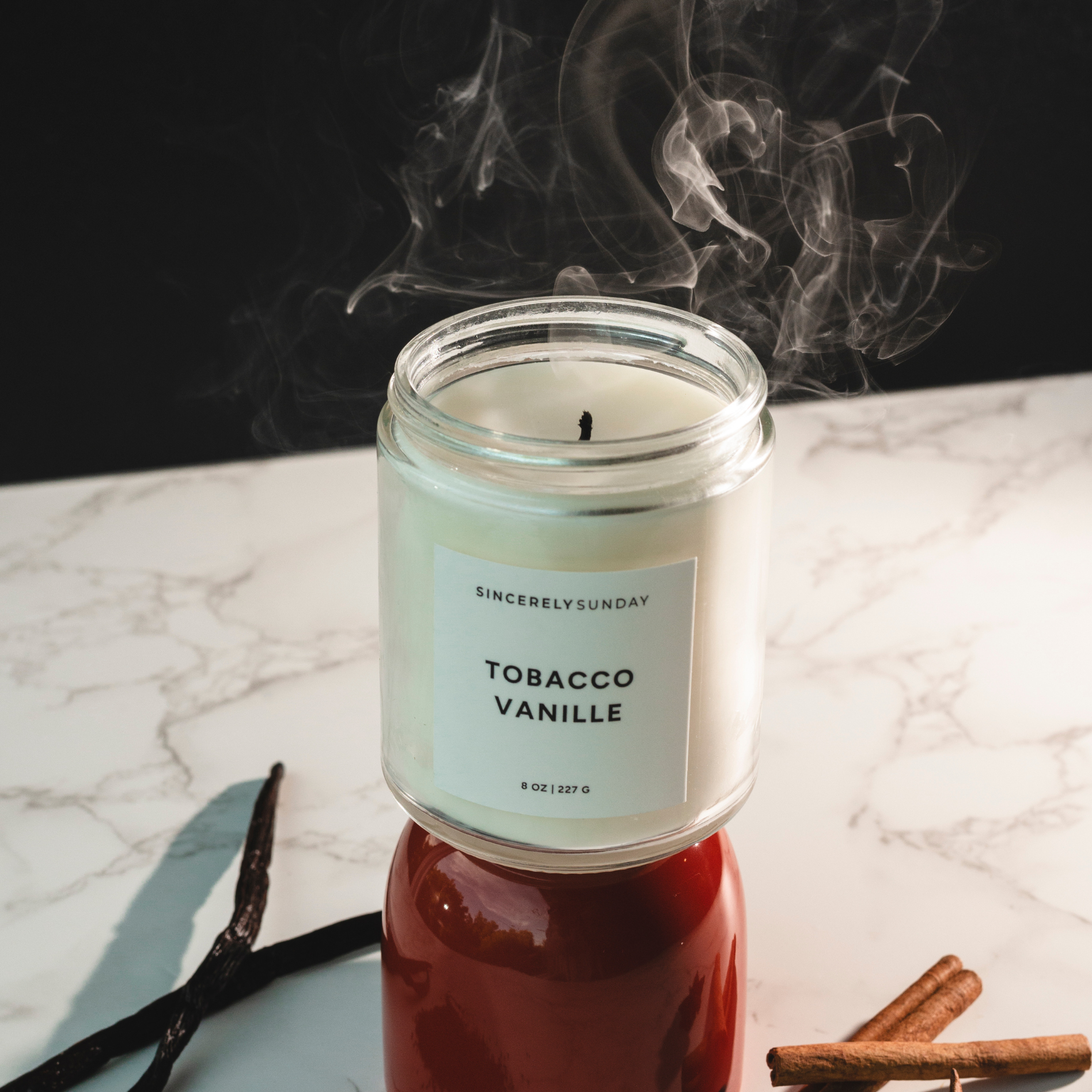 Candle labeled 'Tobacco Vanille' with smoke on a marble surface