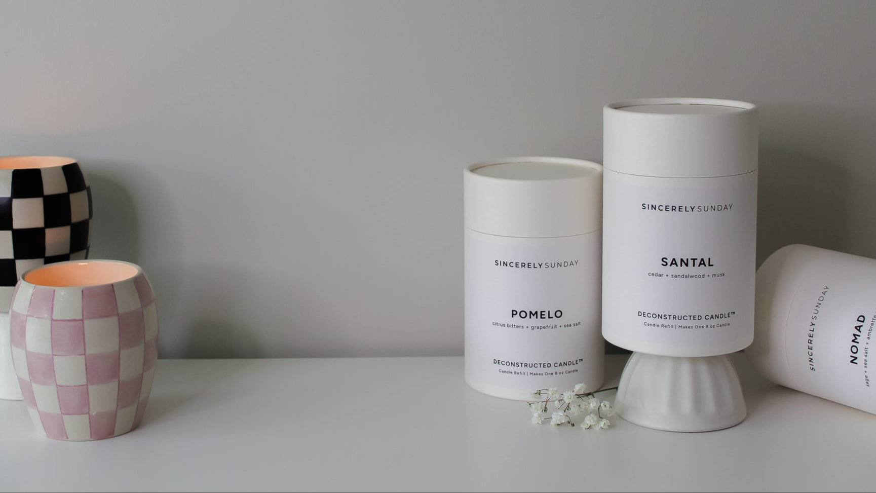 Three candle refill kits in white tubes displayed beside two lit checkered candles, showing finished candle results.