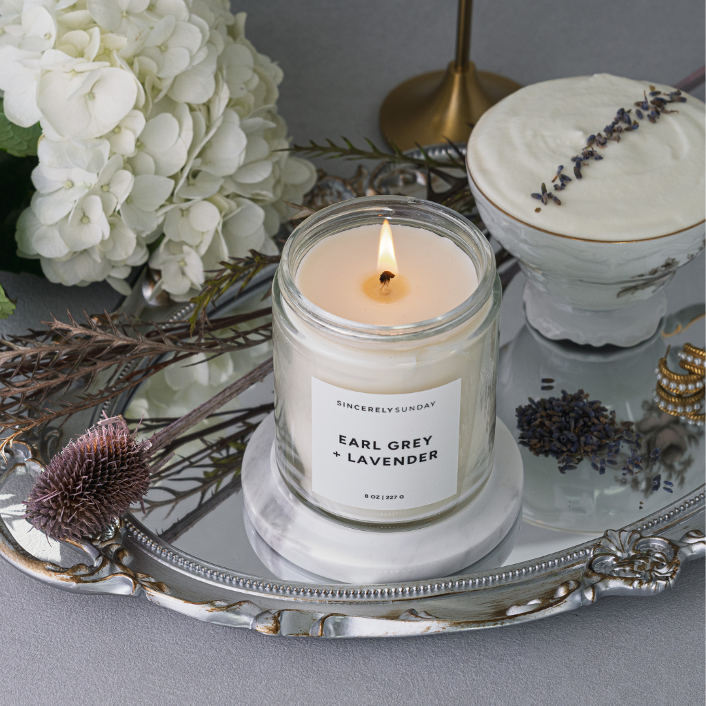 Candle labeled 'Earl Grey & Lavender' on a decorative tray with flowers and a cake.