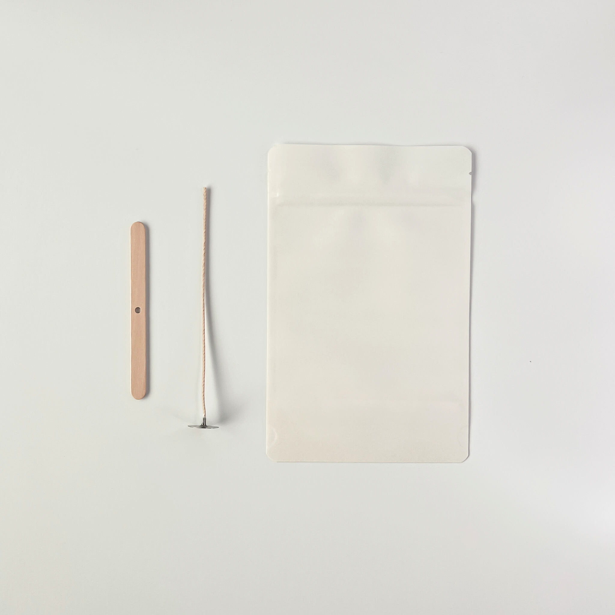 top down view of wooden wick, wick holder, and white pouch tools on a light gray background