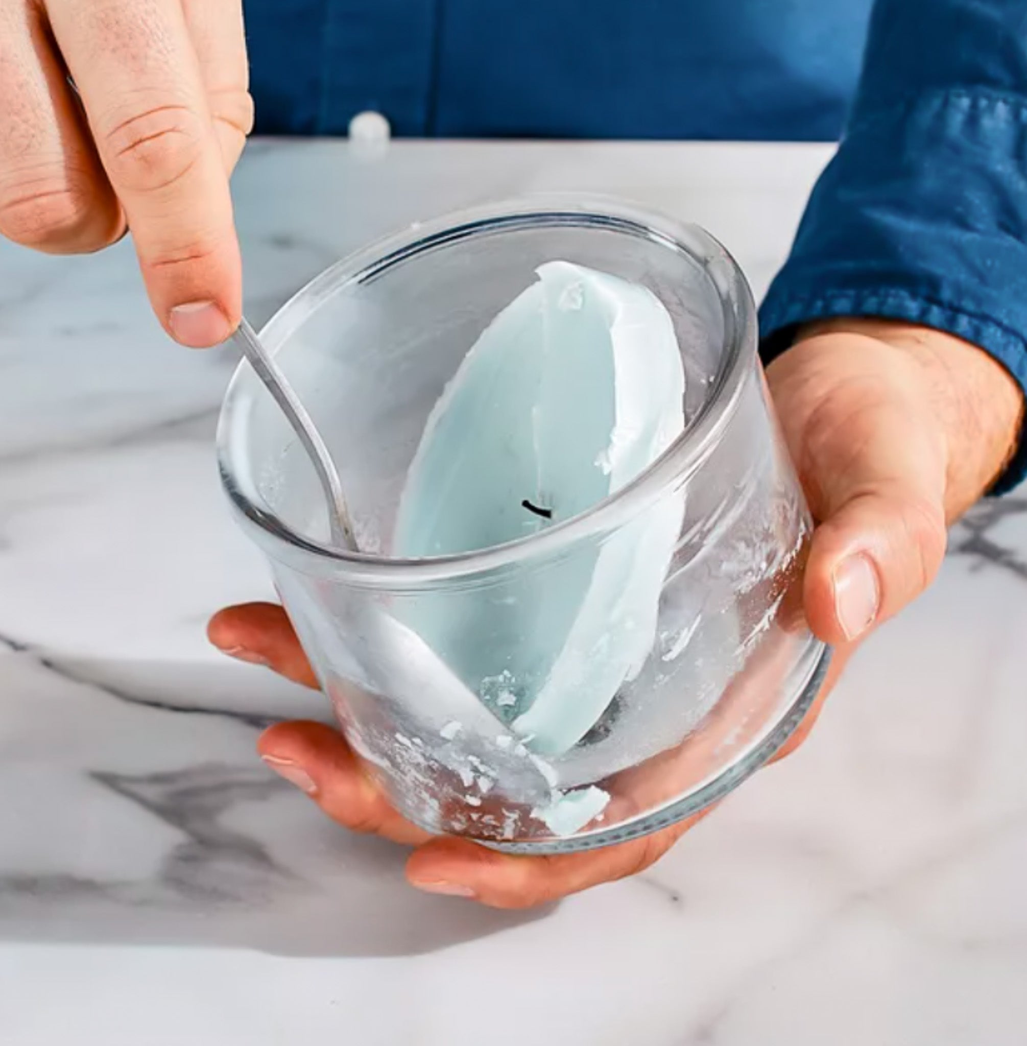 Person holding a candle, scooping the frozen leftover wax out