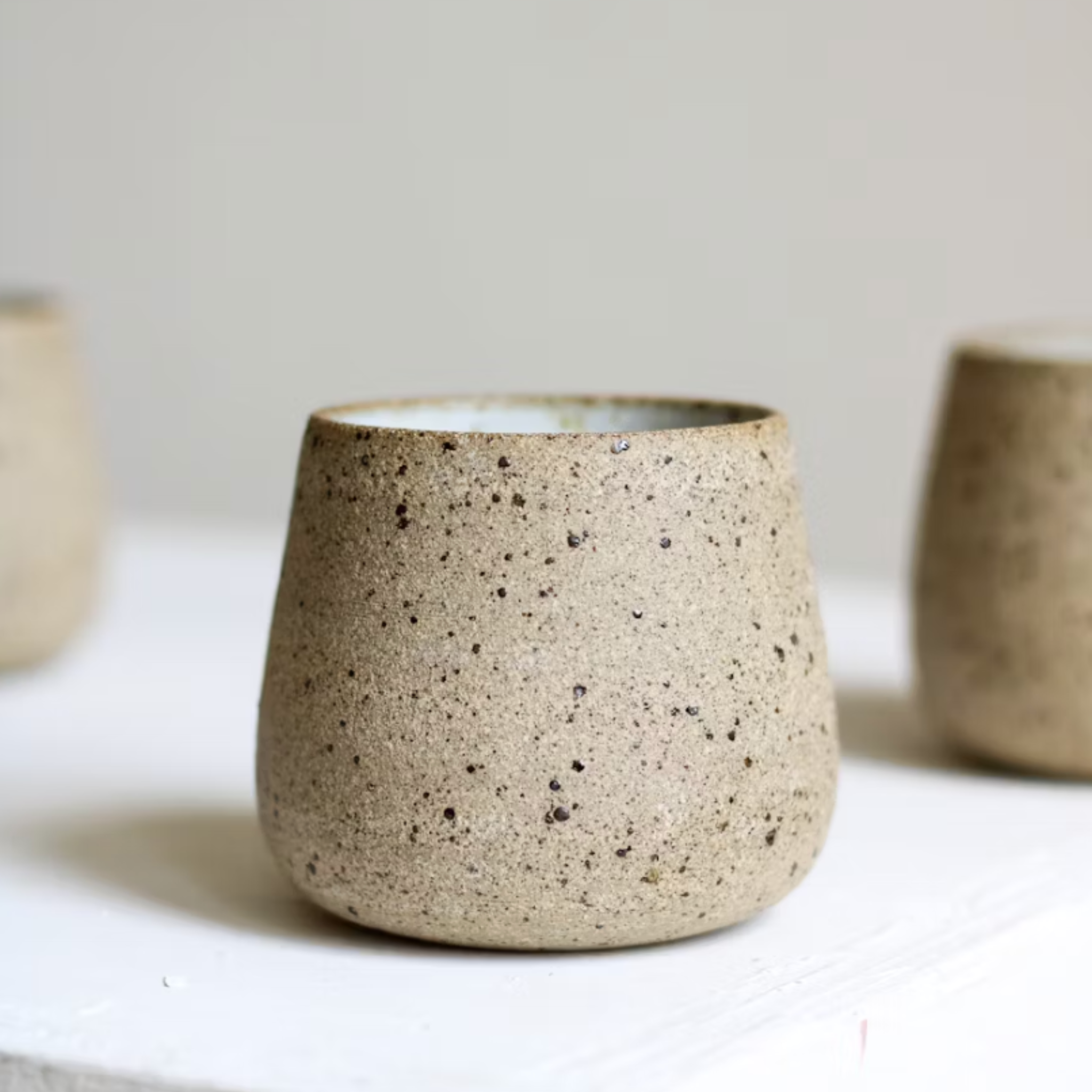 Speckled ceramic cups on a light surface with a neutral background