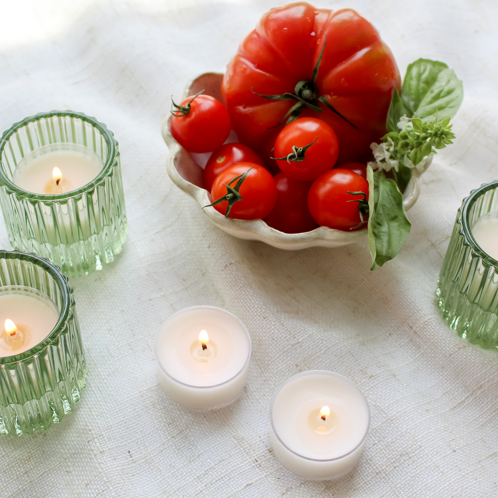 Tea light candles next to scalloped dish with fresh tomatoes in a decorative setup.