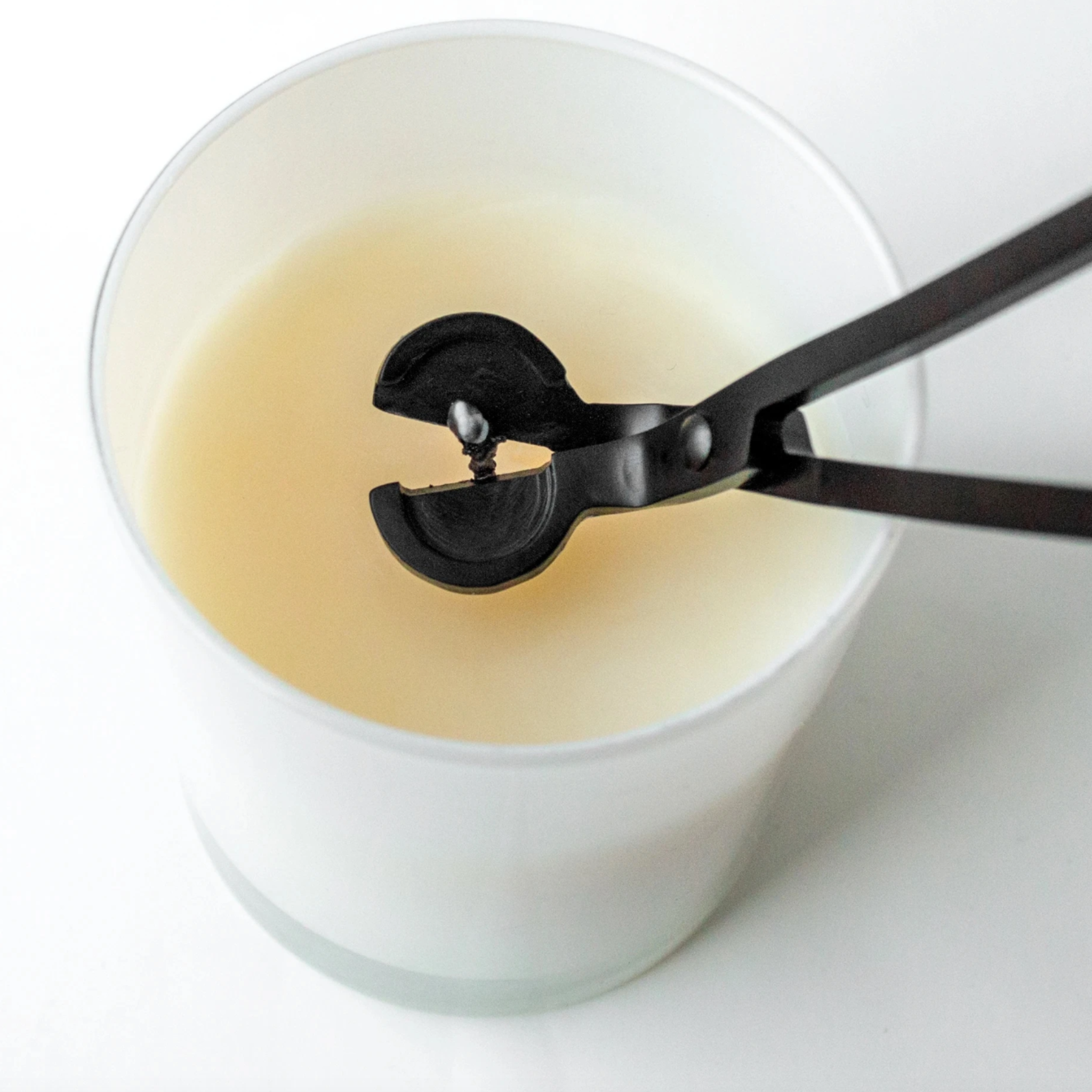 Black candle wick trimmer held above a white candle, ready to trim the wick.